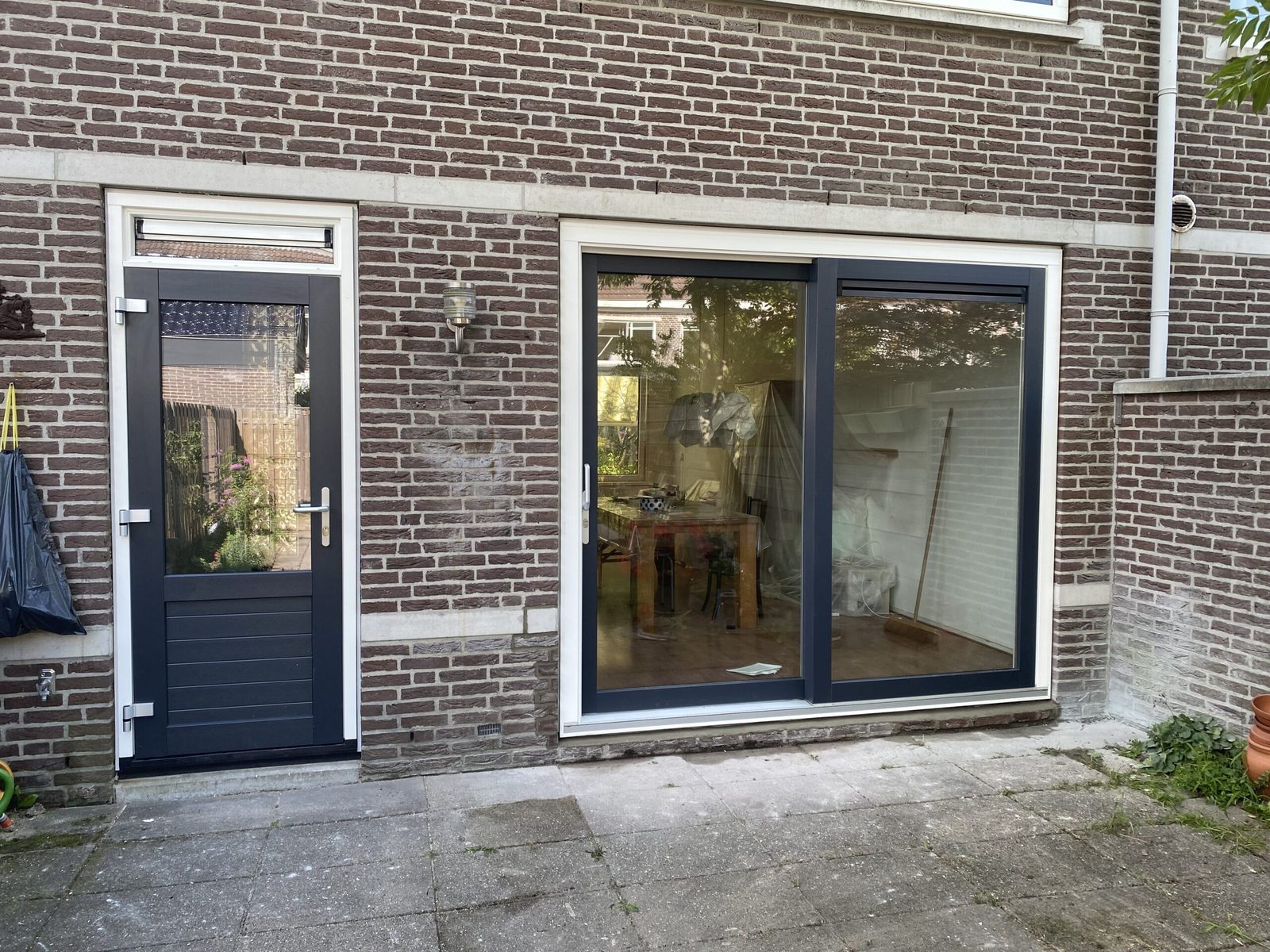 Antraciete achterdeur en schuifpui met witte omlijsting in een bakstenen gevel