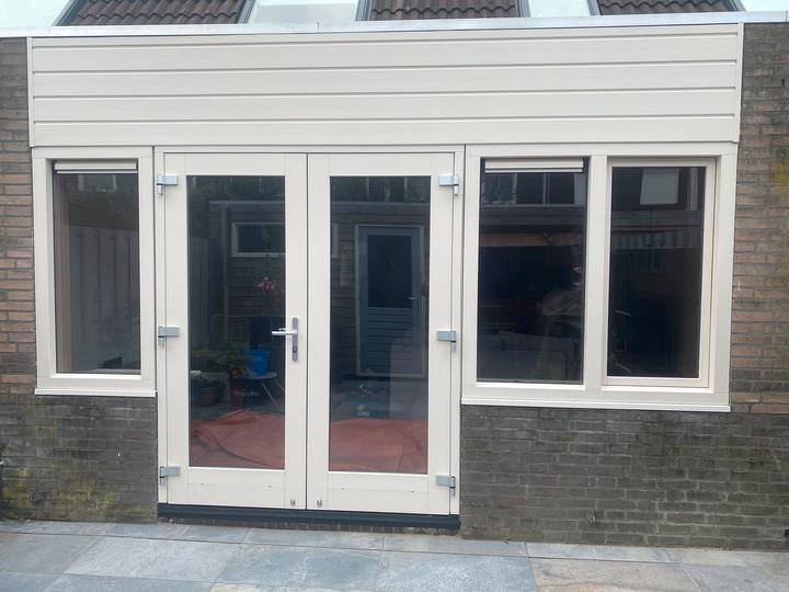 Crème kozijnen met openslaande deuren en zijramen onder lichte gevelbekleding