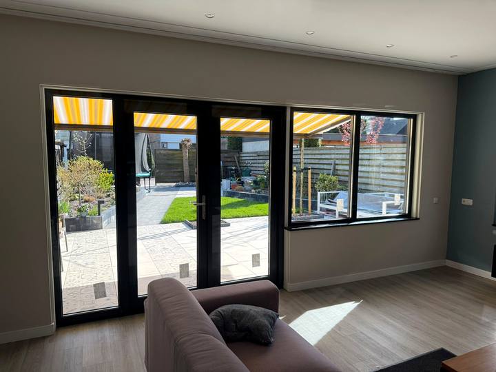 Antraciete openslaande deuren met ramen, van binnenuit gezien met de tuin in de zon