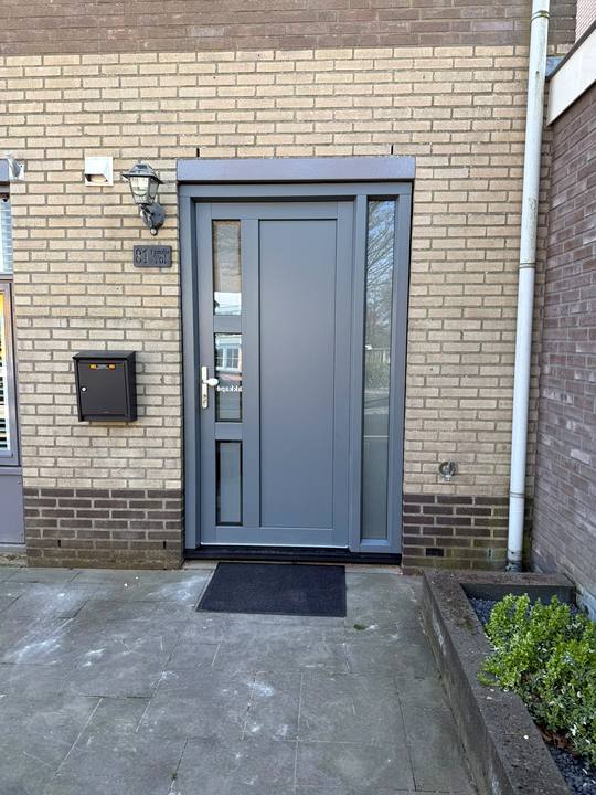 Grijze voordeur met glasstroken en een zijlicht onder een luifel