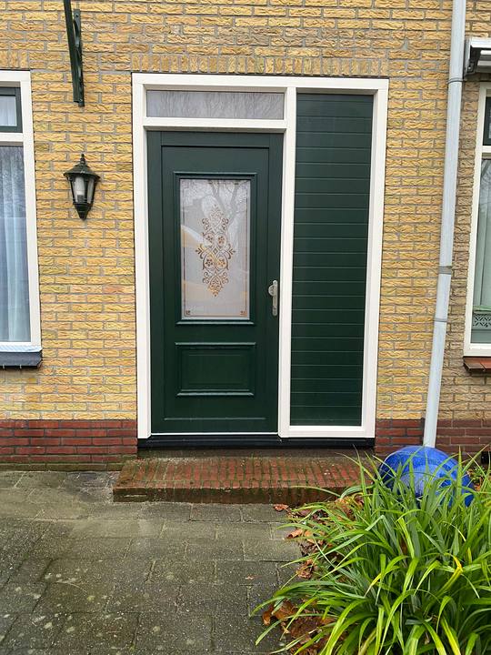 Donkergroene voordeur met decoratief glas en een vast zijpaneel