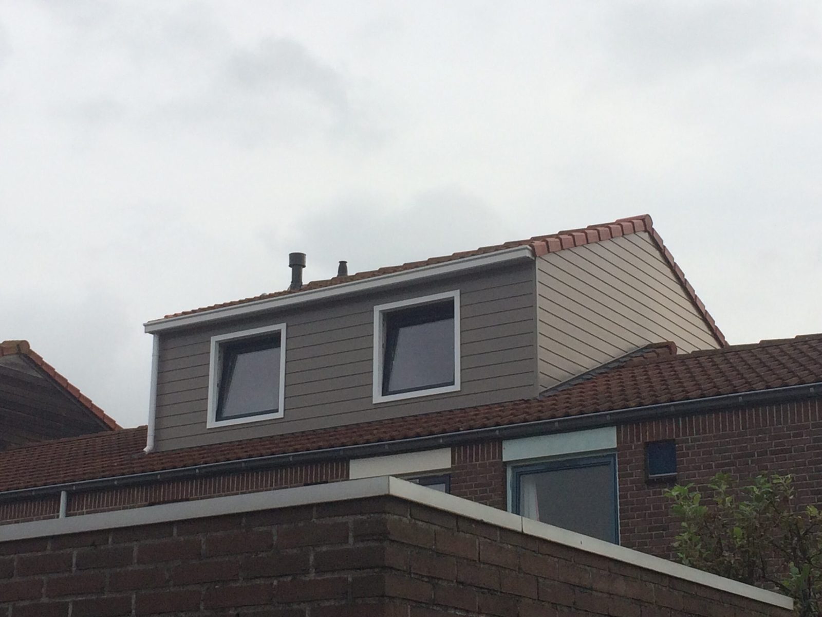 Dakopbouw met taupe gevelbekleding en witte kozijnen op een woning