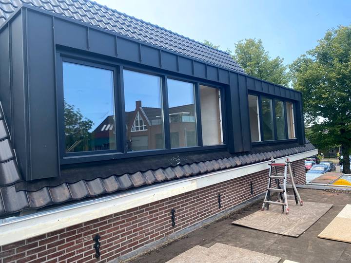Brede antraciete dakkapel met grote glasvlakken op een pannendak