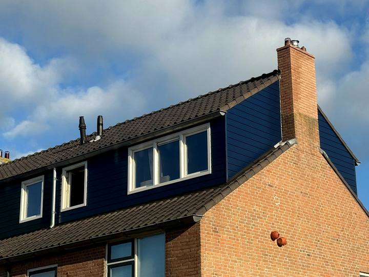 Dakopbouw met blauwe gevelbekleding en witte kozijnen op een bakstenen hoekwoning