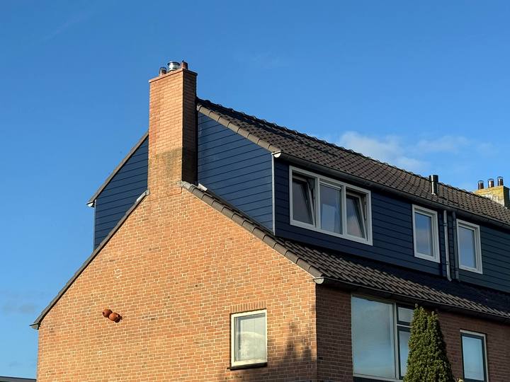 Dakopbouw met blauwe gevelbekleding en witte kozijnen, gezien vanaf de kopgevel