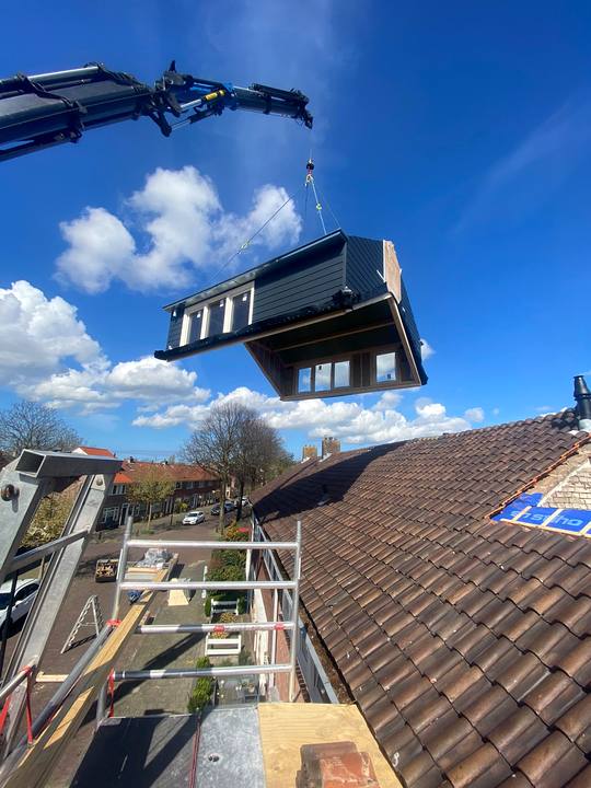 Prefab dakopbouw hangt aan de kraan boven het dak, klaar om te plaatsen