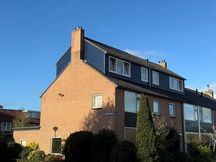 Dakopbouw op een hoekwoning met blauwe gevelbekleding, gezien vanaf de straat