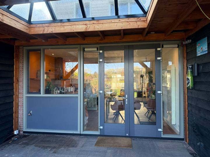 Grijsblauwe kozijnen en deuren onder een houten overkapping met glazen dak