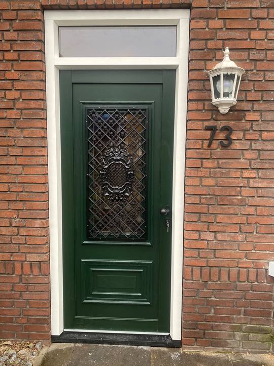 Donkergroene klassieke voordeur met smeedijzeren rooster en bovenlicht